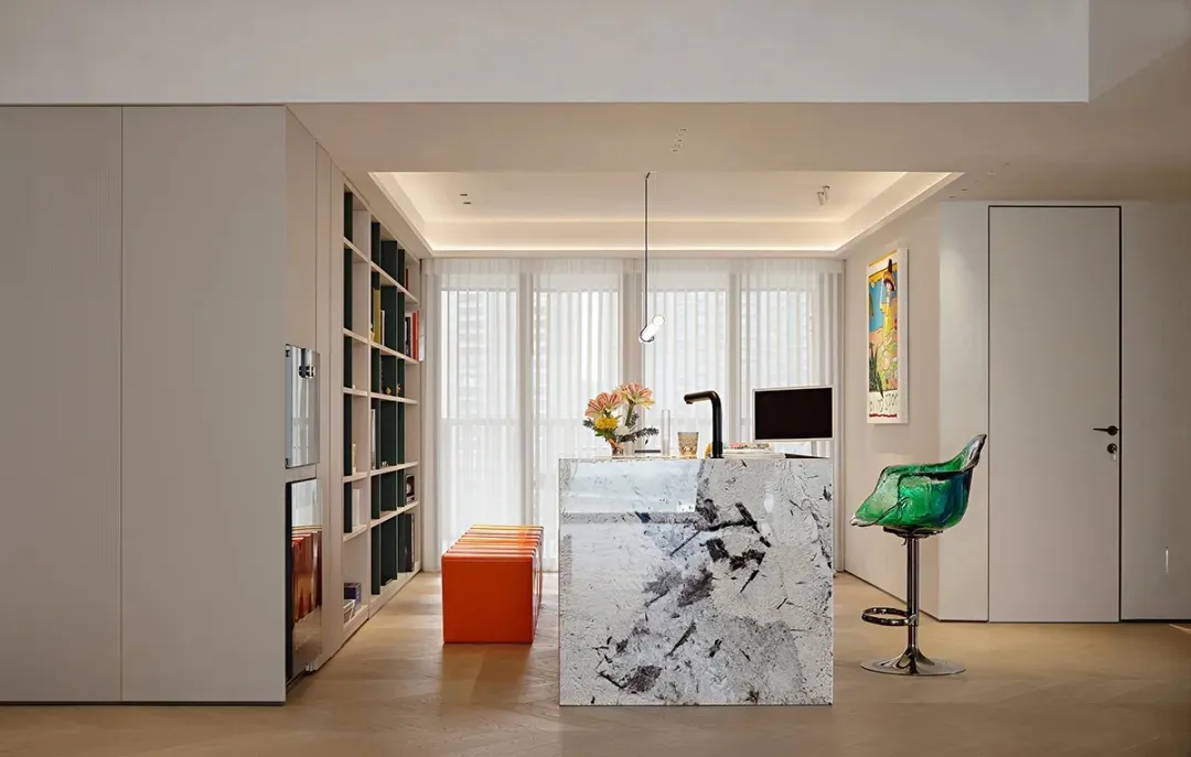 A contemporary kitchen with a white marble island, white cabinets, and an orange stool.