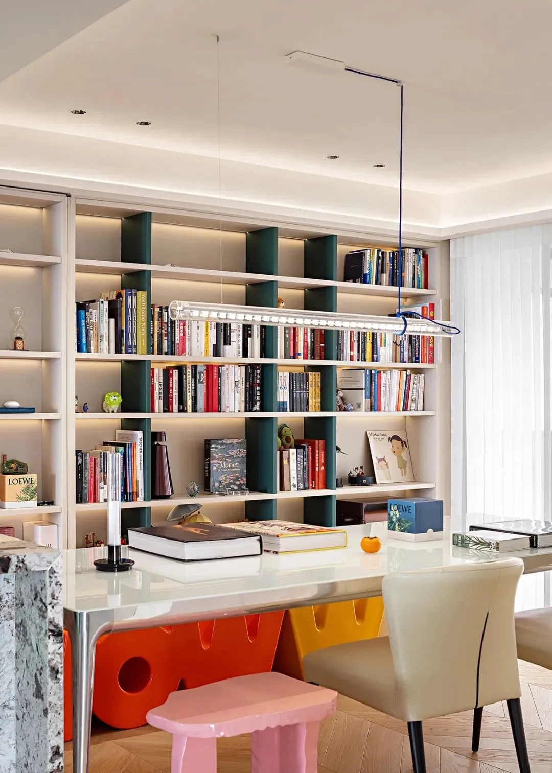 A contemporary home library with steel shelving, colorful stools, and a white desk.