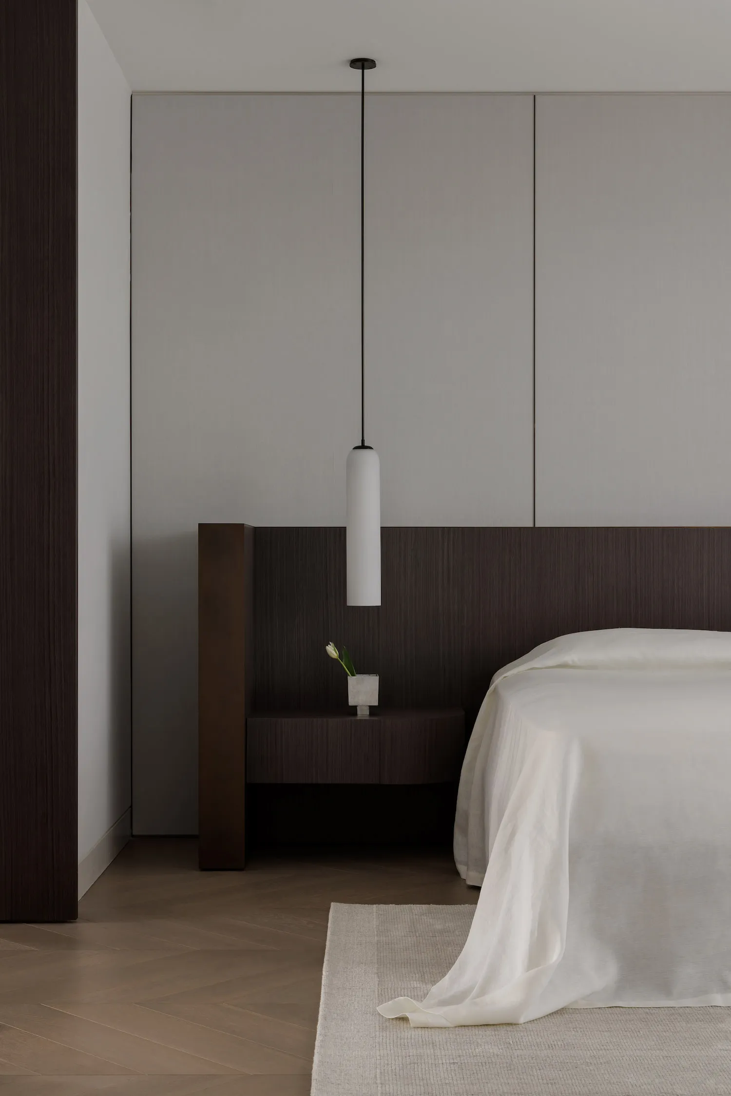 A minimalist bedroom with wooden furniture and soft textiles, featuring a floating nightstand with a vase of tulips and a sle