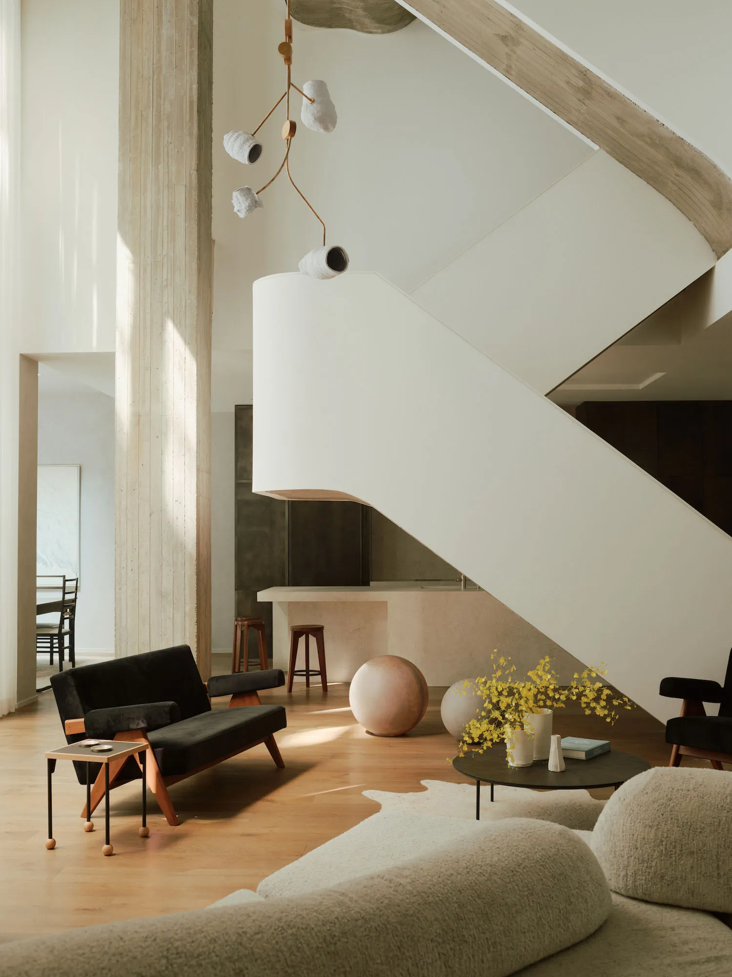 A modern minimalist living room featuring concrete walls, wood accents, and a large staircase.