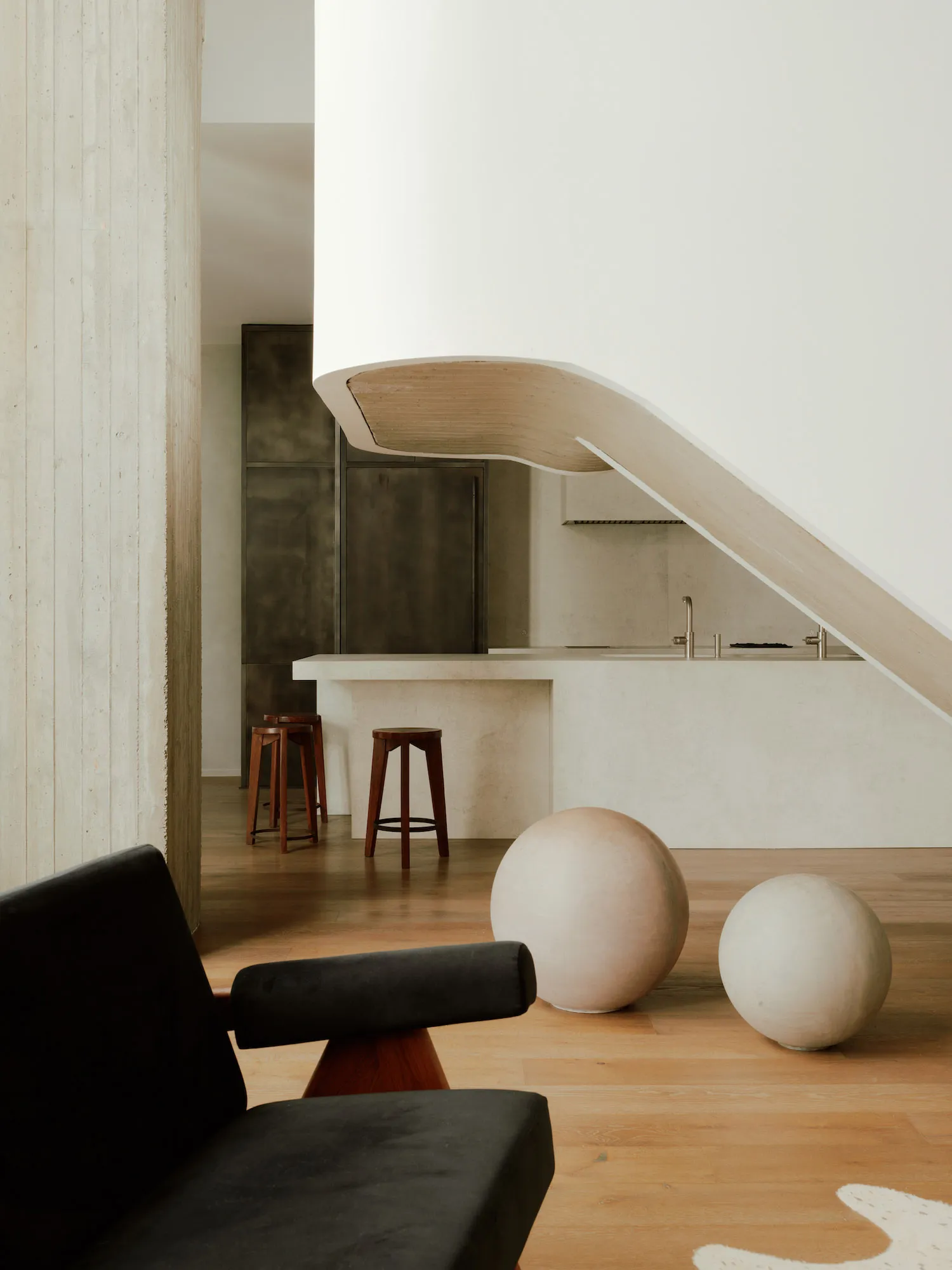 A modern minimalist kitchen featuring a sleek concrete countertop and wooden stools.