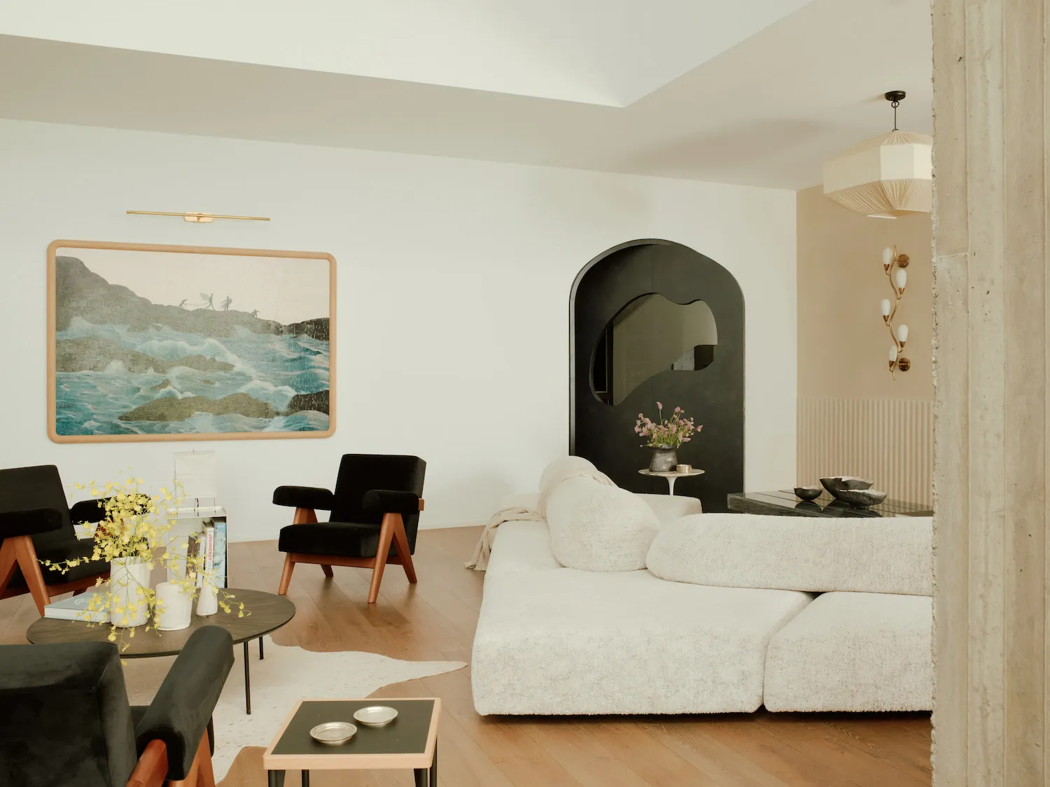 A modern living room featuring a white sofa, black armchairs, and a wooden floor with a cowhide rug. The decor includes a lar