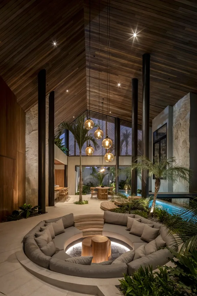 Modern living room with circular seating area, concrete floor, wood accents, and glass windows.