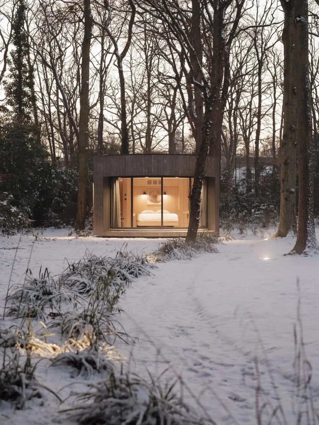 A minimalist cabin with wood and glass exterior in a snowy forest setting.