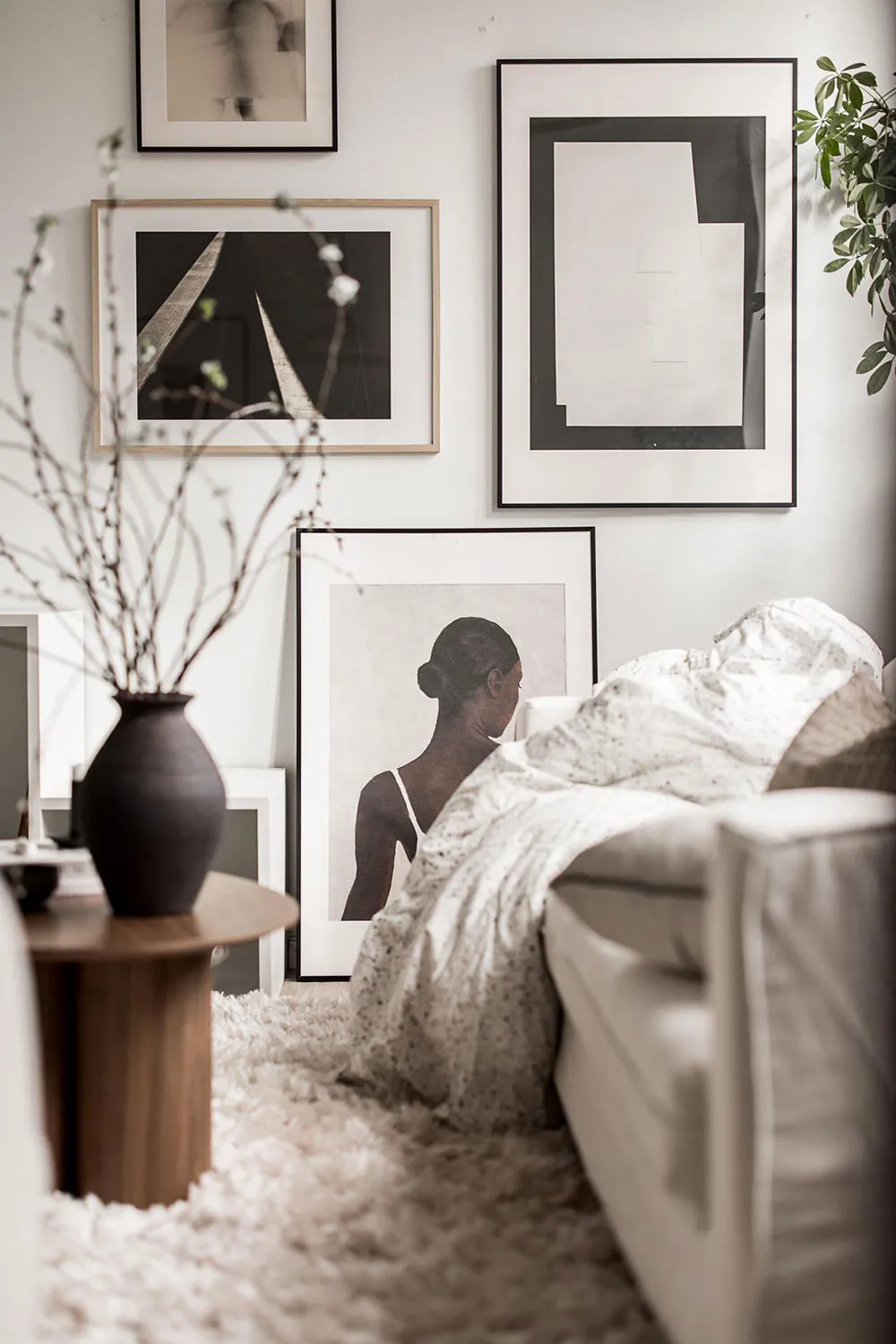 A minimalist living room with a white couch, a round wooden table with a black vase, and a variety of black and white framed