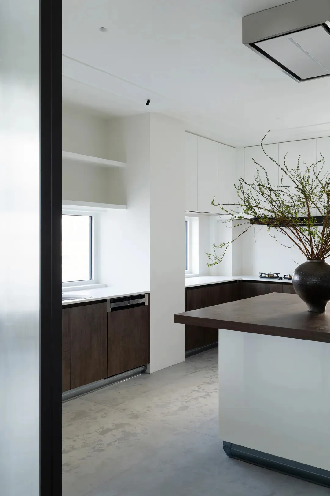 Modern kitchen with minimalist design featuring clean lines, white countertops, dark wood cabinetry, and natural light from t