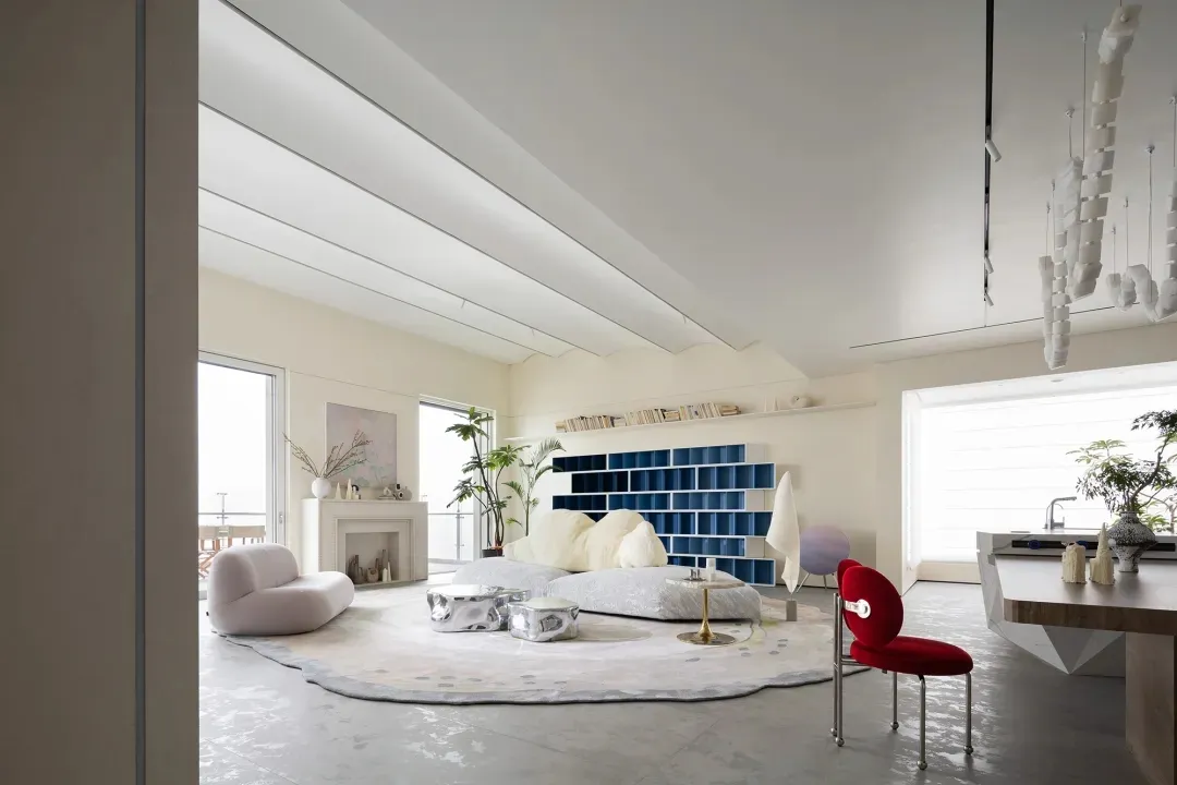A modern living room with concrete flooring, minimalist furniture, and a large bookshelf.