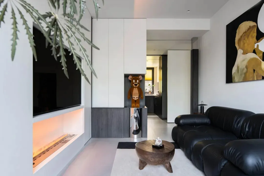 A modern living room featuring a black leather sofa, a wooden coffee table, and an ethereal fireplace with orange lighting, a
