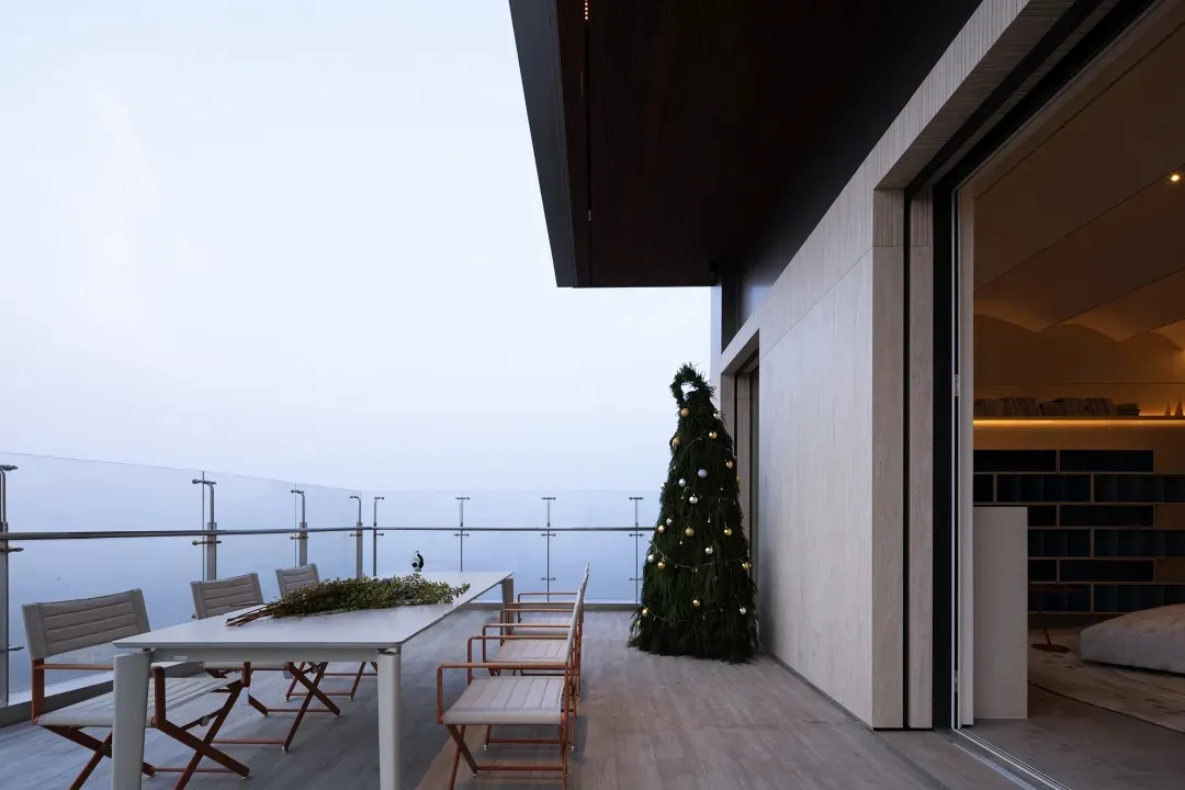 Modern residential balcony furnished with a white dining table, chairs, and a Christmas tree with lights and ornaments, featu