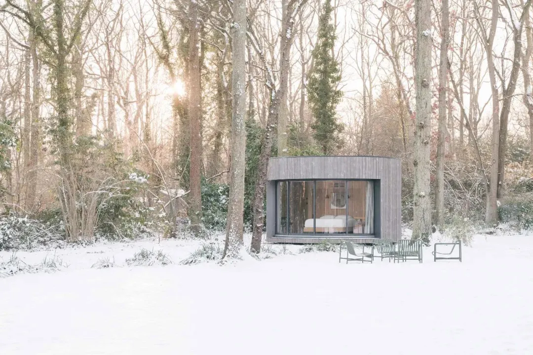 A modern, wooden cabin nestled in a snowy forest, featuring large glass windows and minimalistic design.