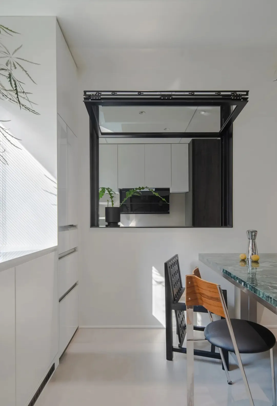 A modern, minimalist kitchen with white cabinets, a white countertop, and a glass window.