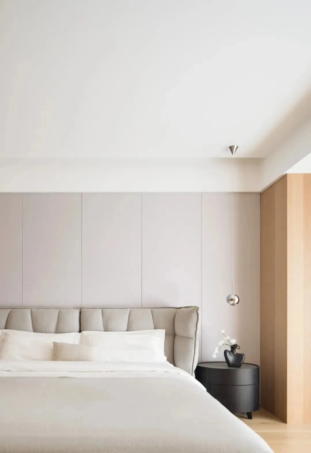 A minimalist bedroom featuring a bed with a fabric headboard against a wall with light gray panels.