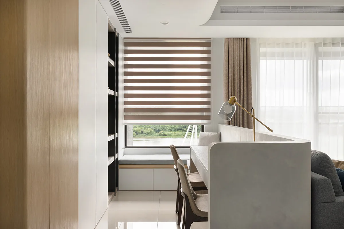 A modern dining room featuring white and light wood elements, with a window overlooking a scenic view and a lamp providing il
