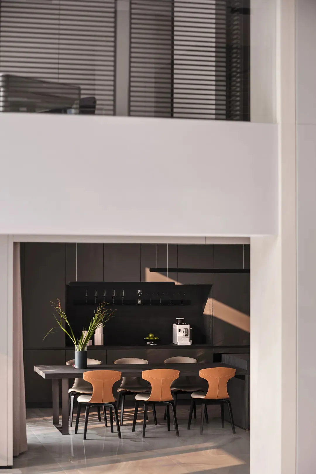 A modern kitchen interior with sleek, minimalist design elements, featuring a dark wooden table, leather and metal chairs, an
