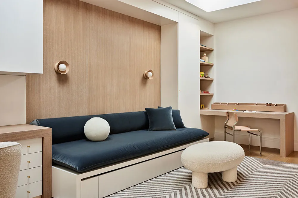 A modern living room with wooden walls, a blue sofa, and a white pouf on a patterned rug.