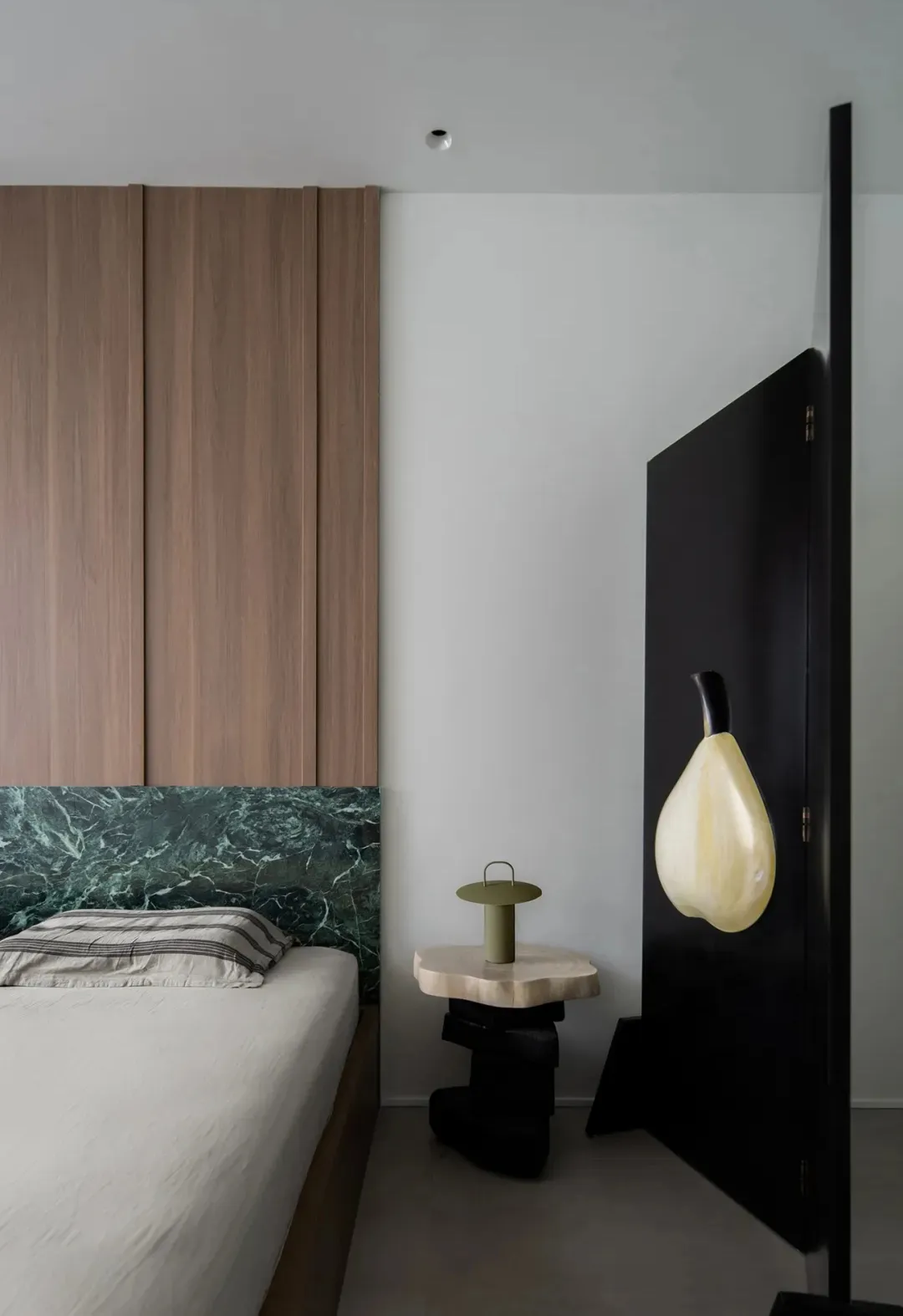 A minimalist bedroom featuring a bed with a marble headboard, wooden wall panels, and a black-framed artwork.