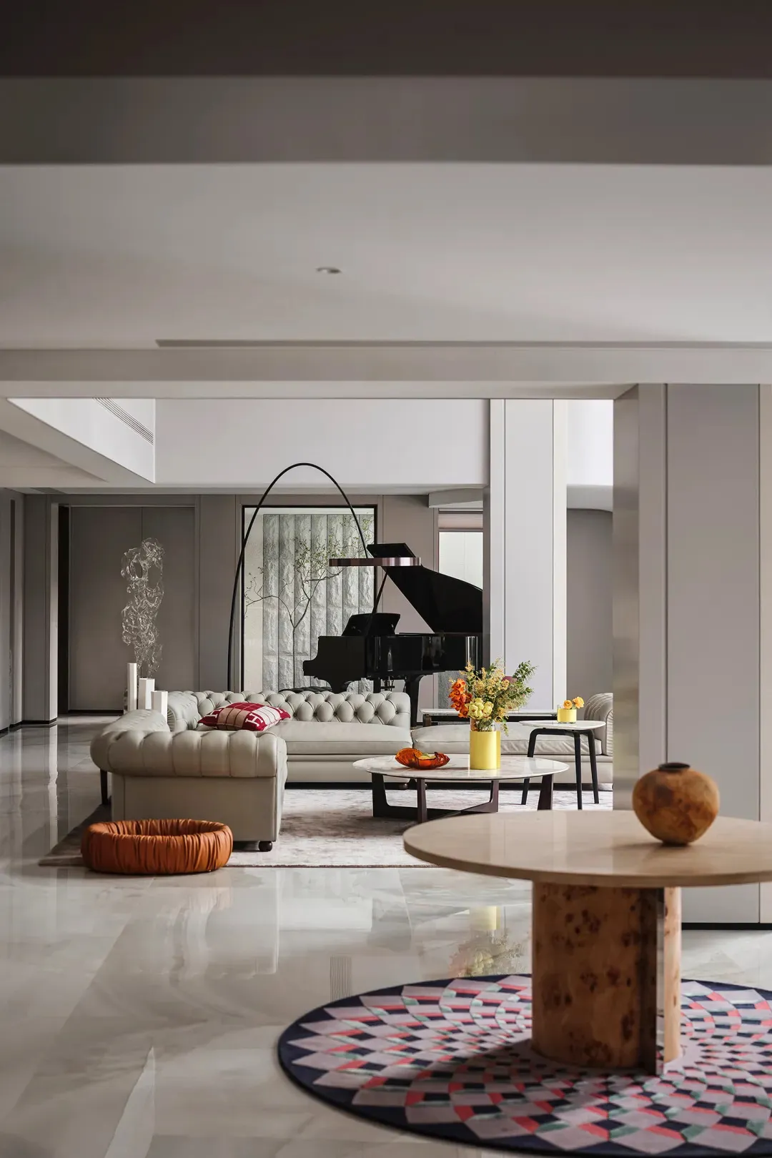 A modern living room featuring marble furniture, including a round table on a colorful patterned rug and a piano in the backg