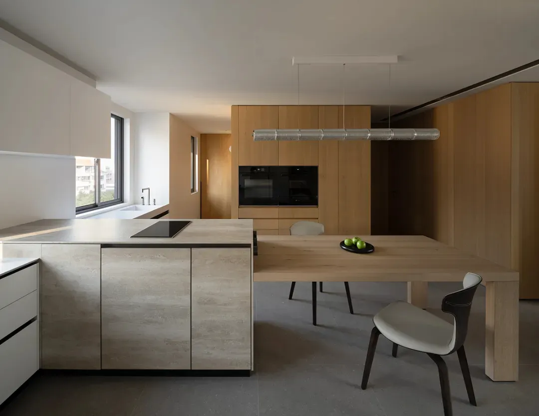 A modern kitchen featuring minimalist design with wooden tables, stone countertops, and metal appliances.