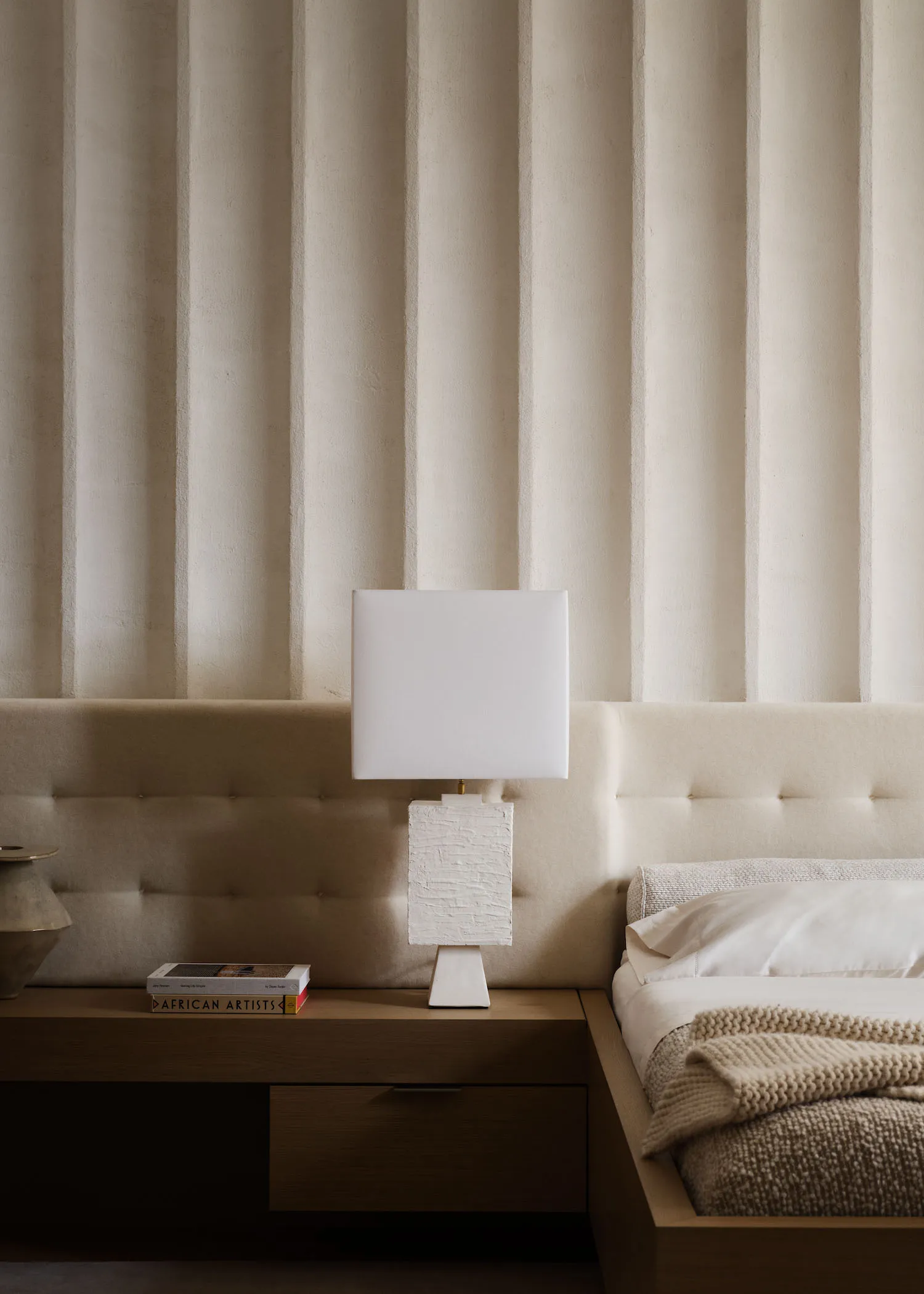 A minimalist bedroom with neutral tones, featuring a bed with a tufted headboard, soft lighting, and simple decor.