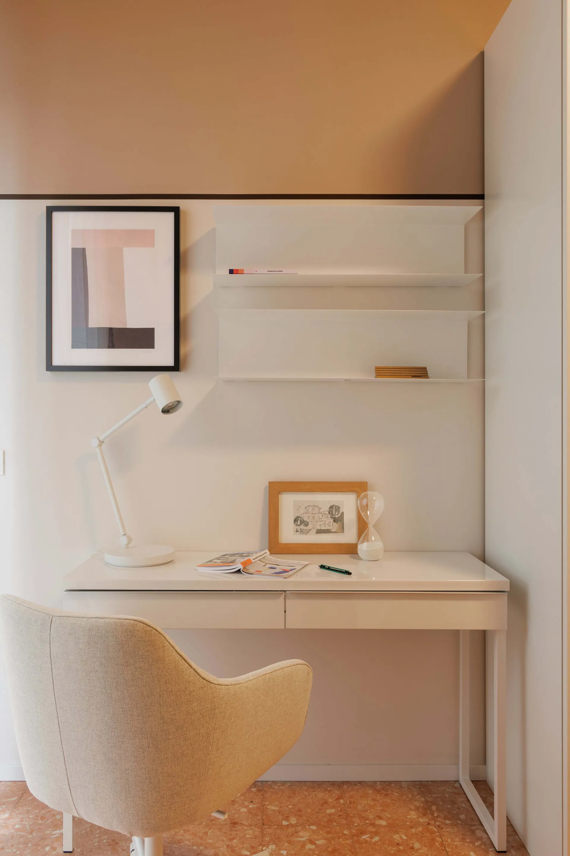 A modern home office setup with a white desk, minimalist shelves, and a beige chair.