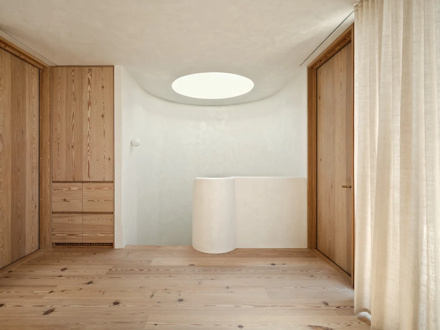 A minimalist bathroom with a white plaster wall and a circular skylight.