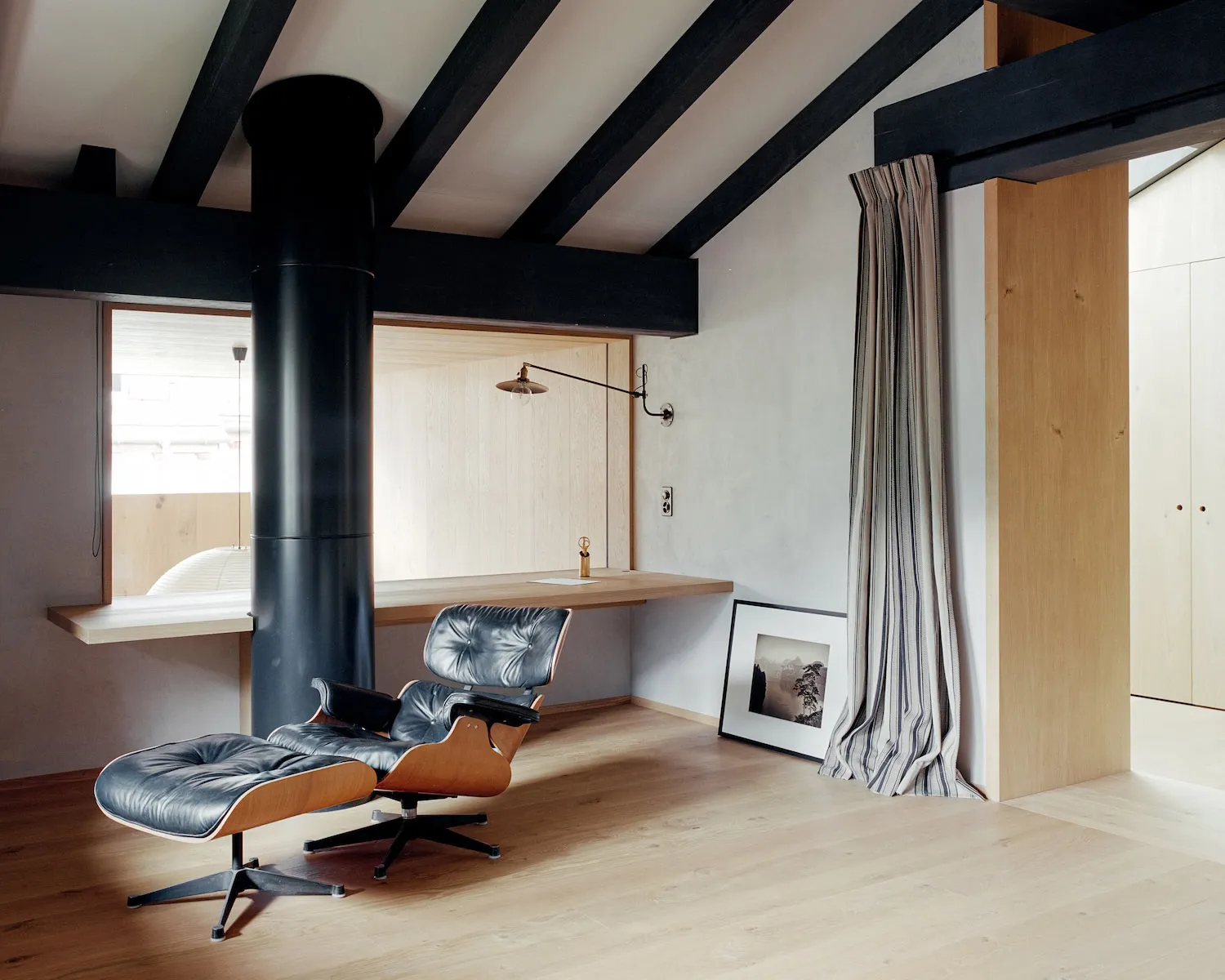 A minimalist residential space with a wooden floor and a black leather sofa.
