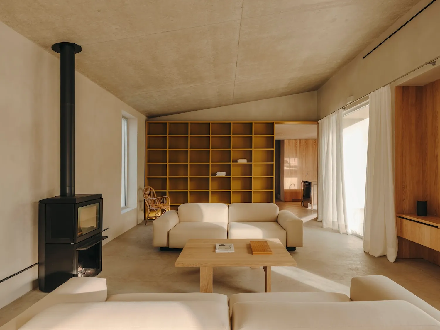 A modern living room with a minimalist design, featuring a concrete ceiling and floor, and a large bookshelf.