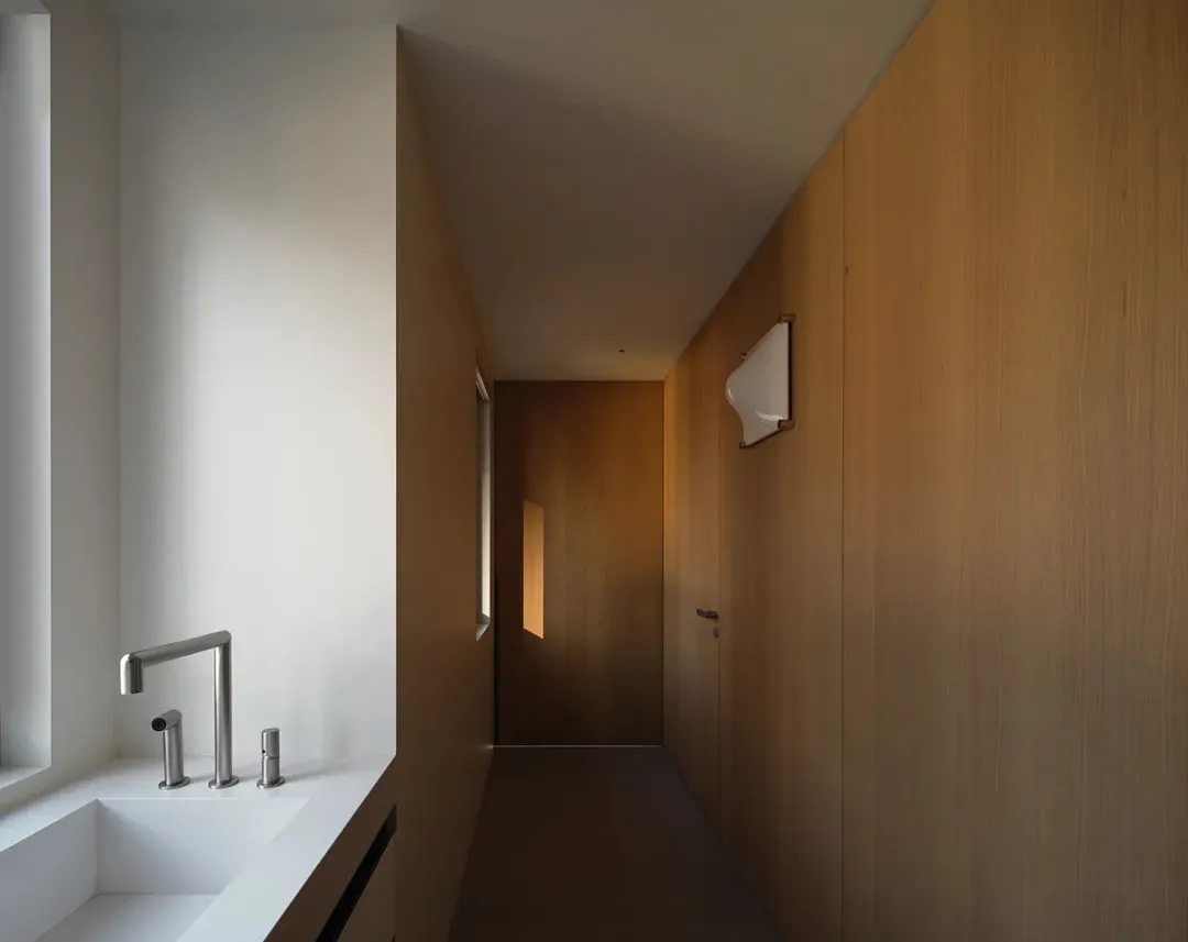 A minimalist bathroom corridor with a white sink and wooden walls.