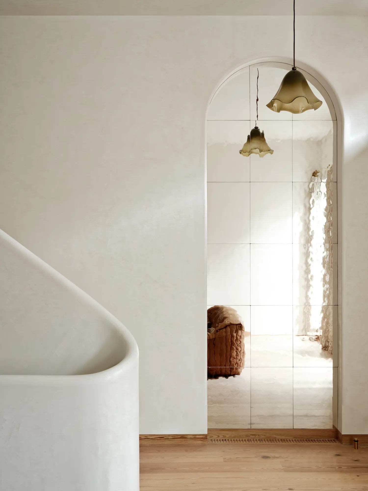 Modern minimalist bathroom with white stone tub and arched mirror.
