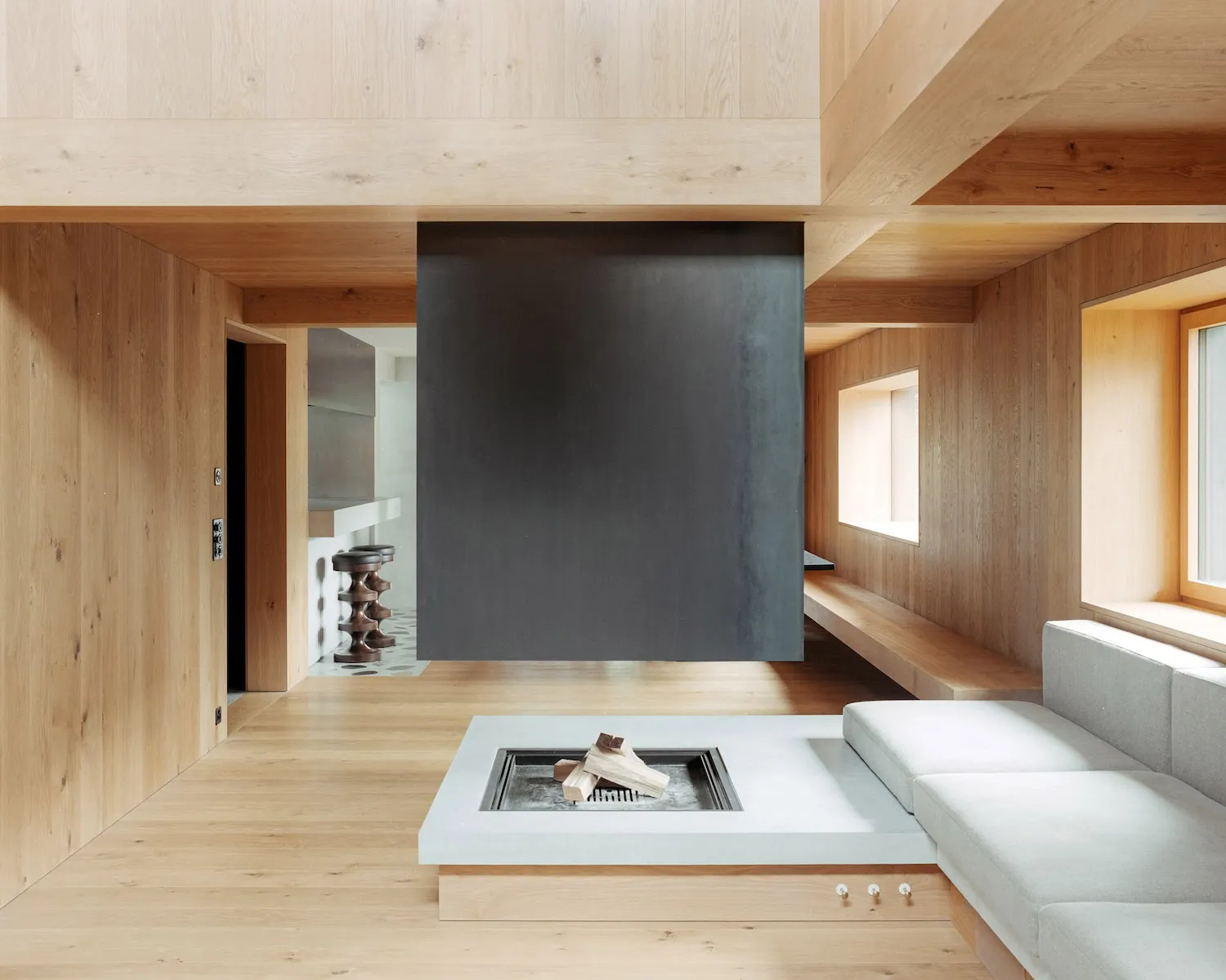 A minimalist living room with wooden walls and ceiling, featuring a white coffee table with a fireplace insert and a white se