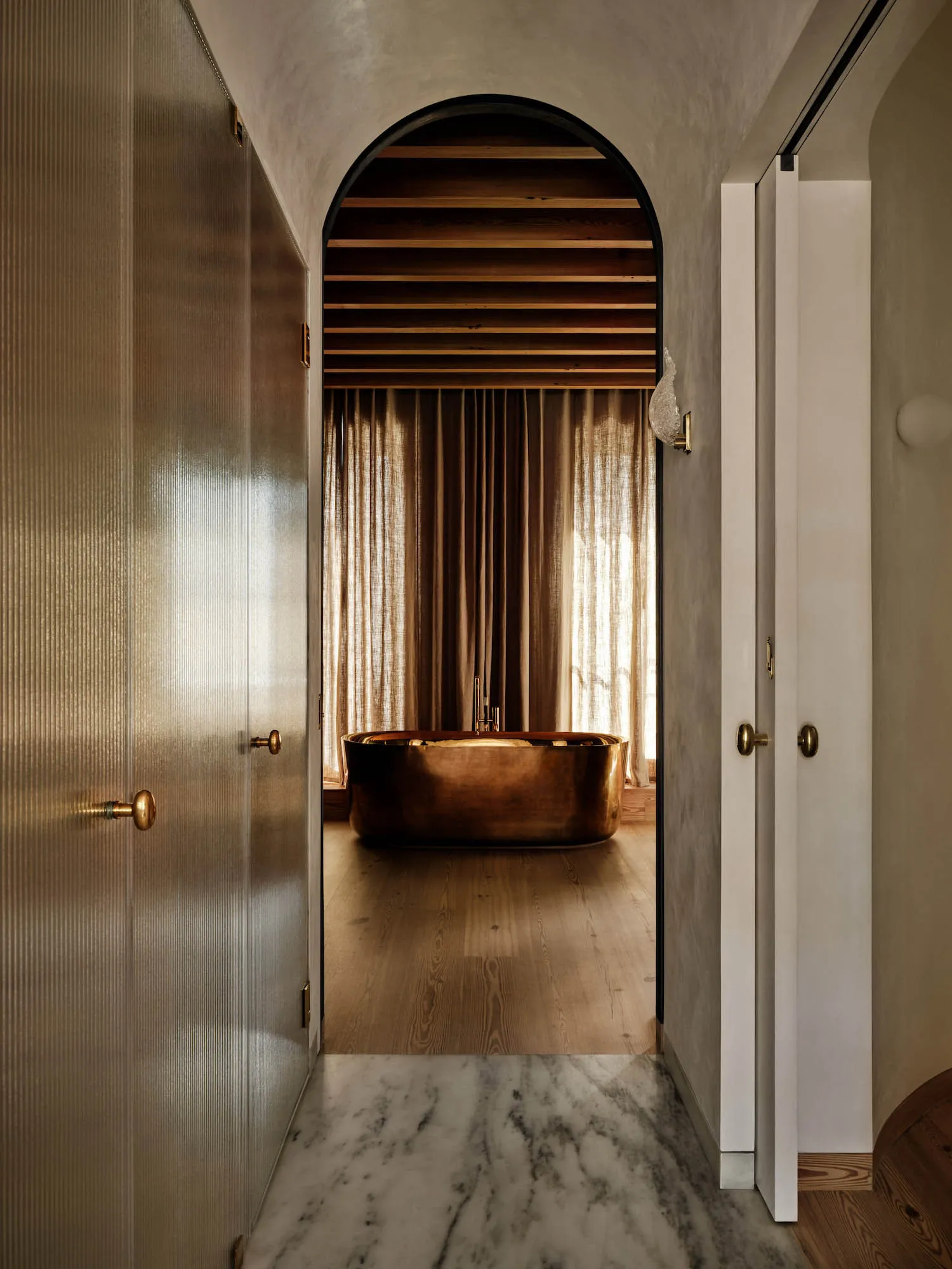 Modern bathroom with a brass bathtub and marble flooring.