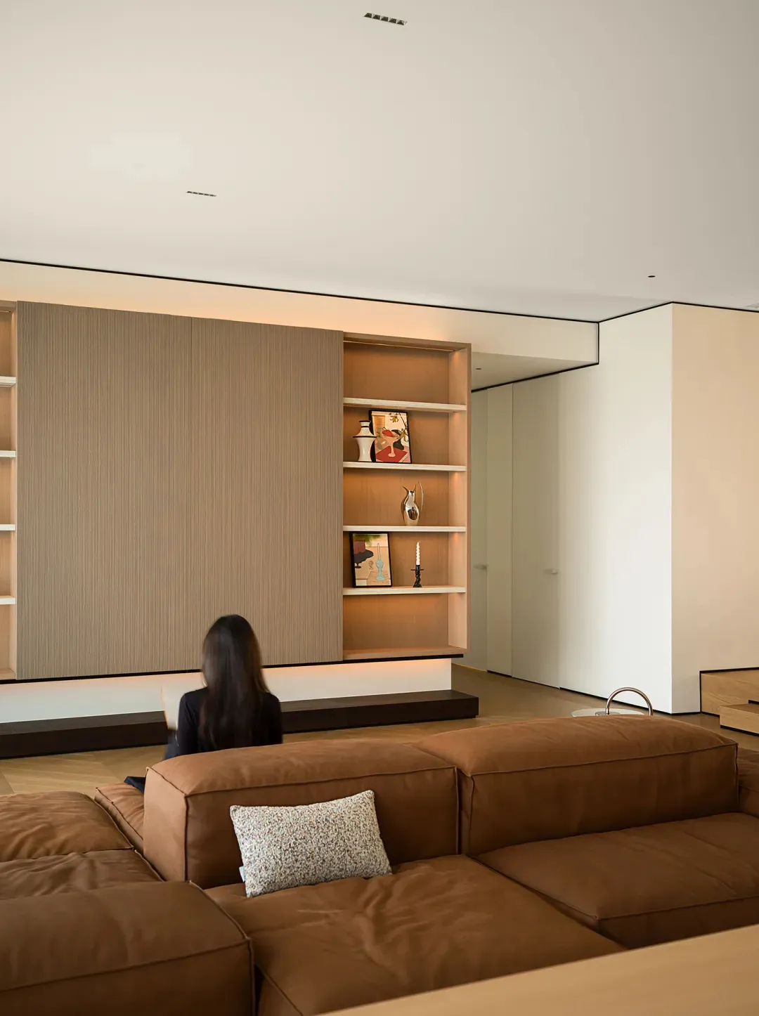 A minimalist living room with a brown leather sectional sofa and a wooden wall shelf.