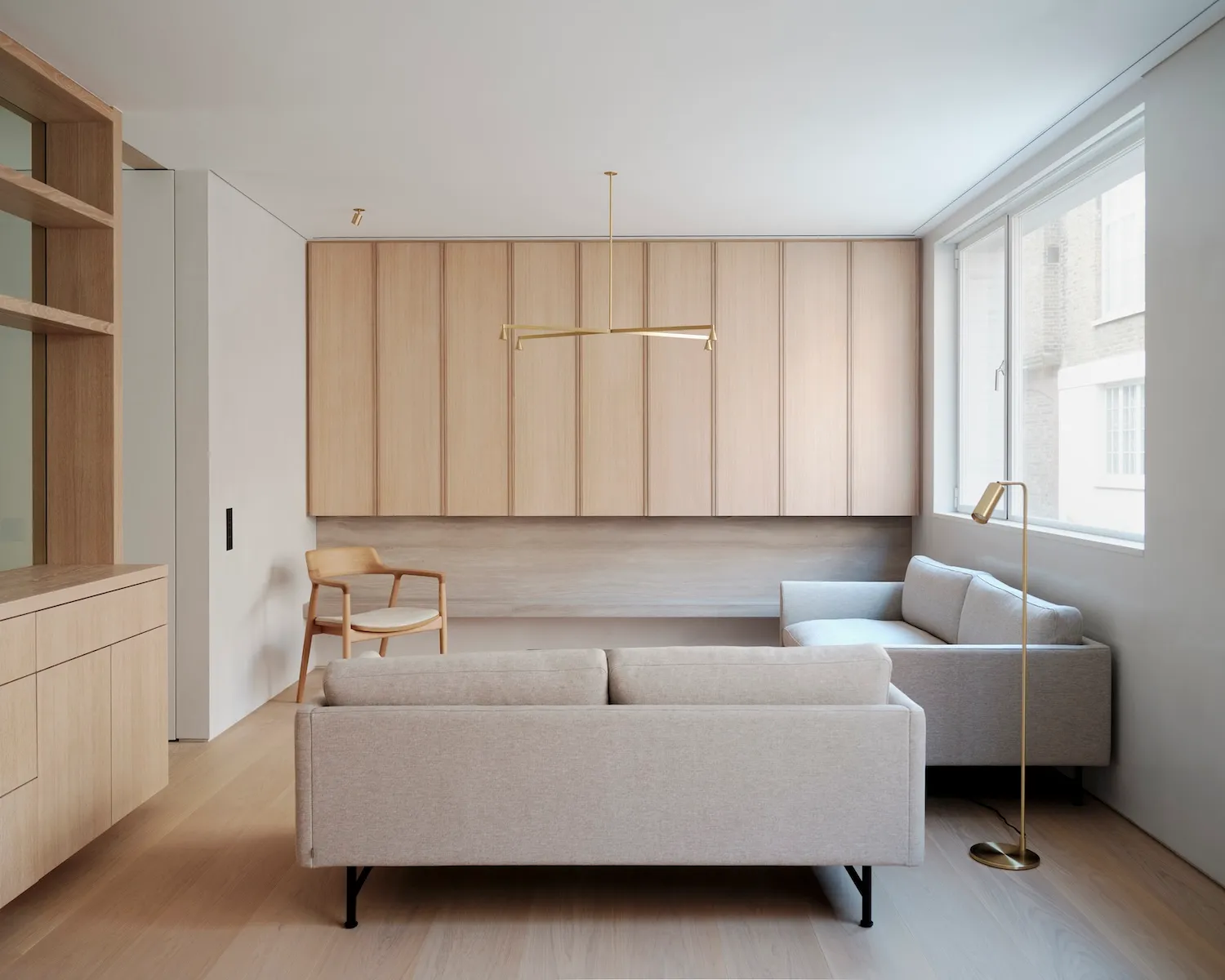 Modern minimalist living room with light-colored wooden flooring, light-colored sofas, and a wooden counter with built-in sto