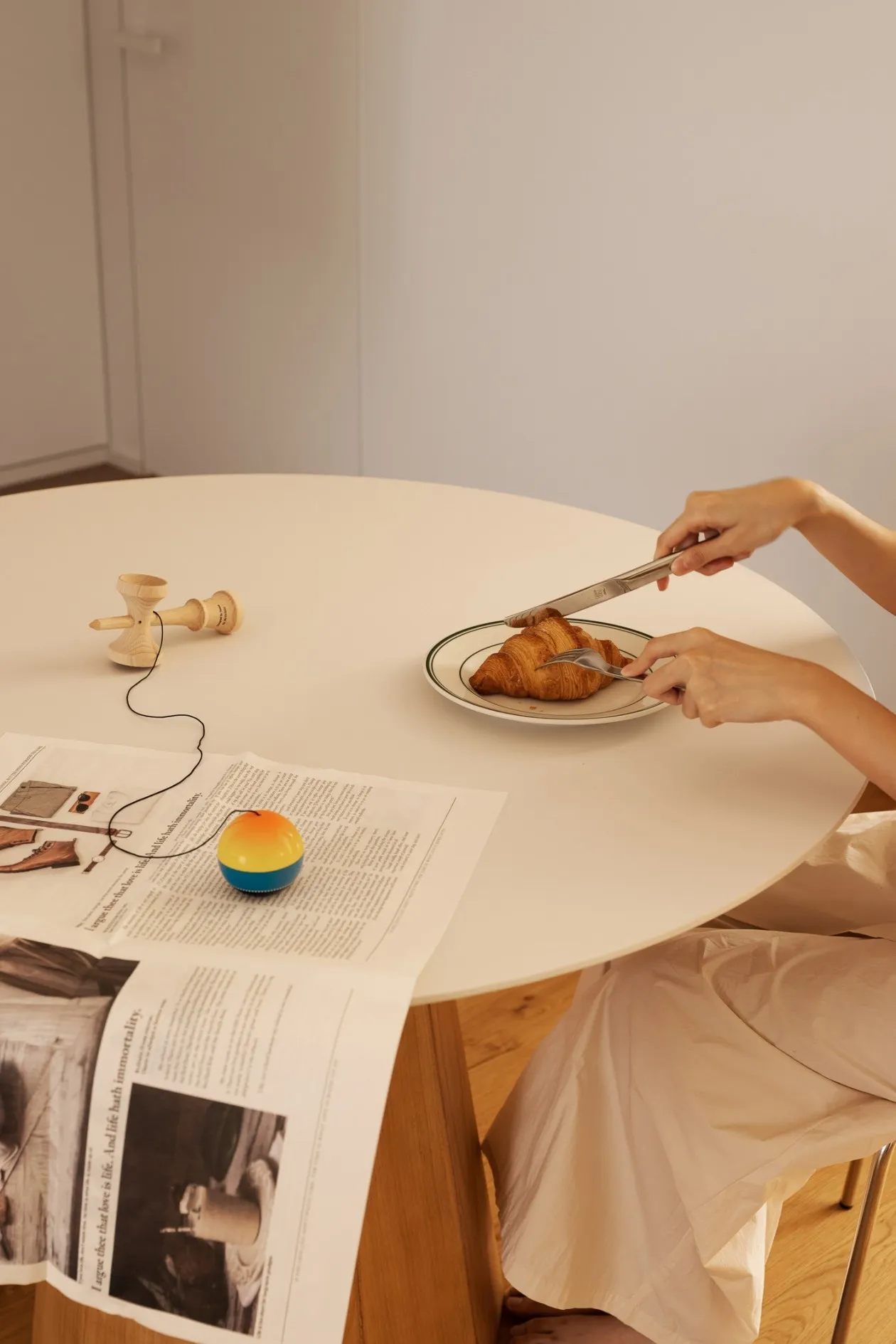 Hands cutting a croissant on a ceramic plate with a knife and fork.