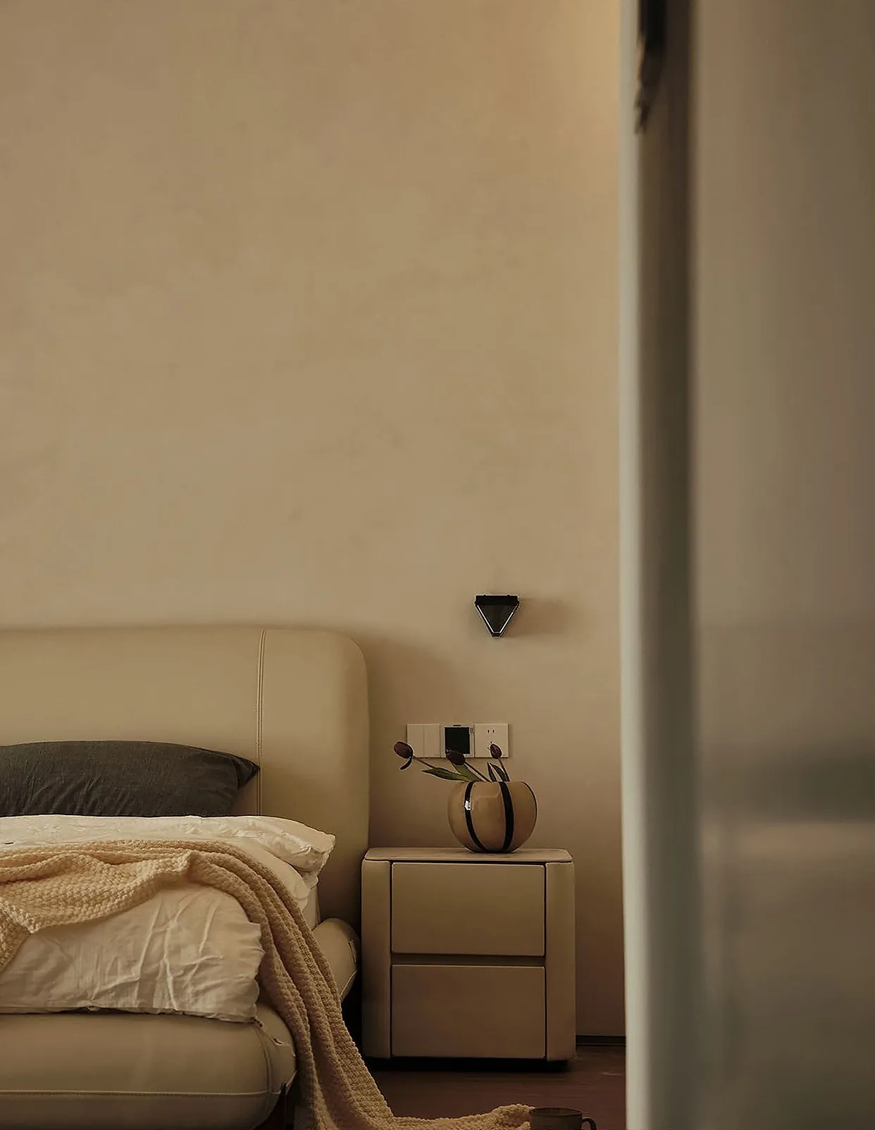Minimalist bedroom featuring a neutral-toned bedside table with a vase and flowers.