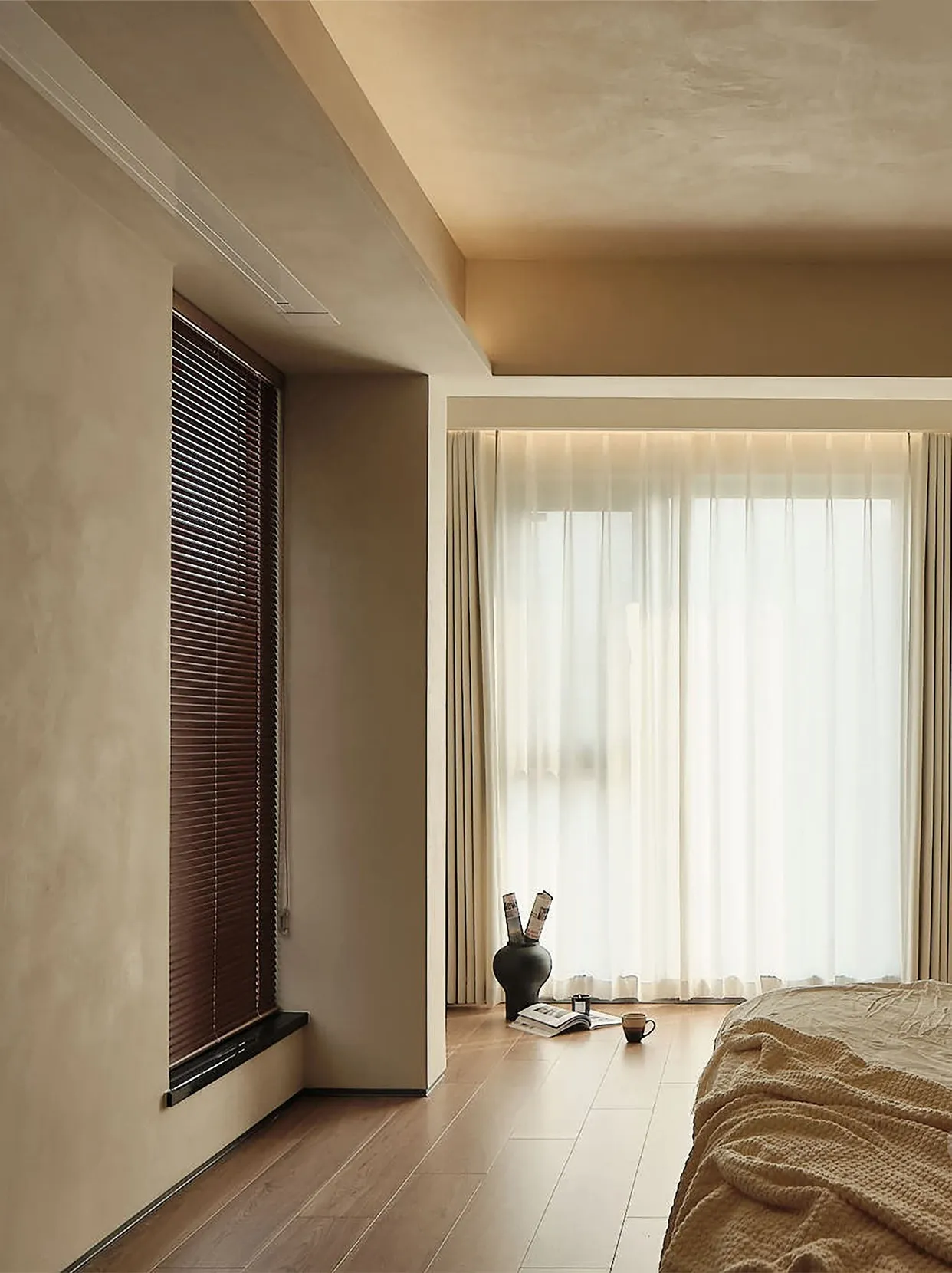 A modern bedroom featuring wooden blinds and sheer curtains