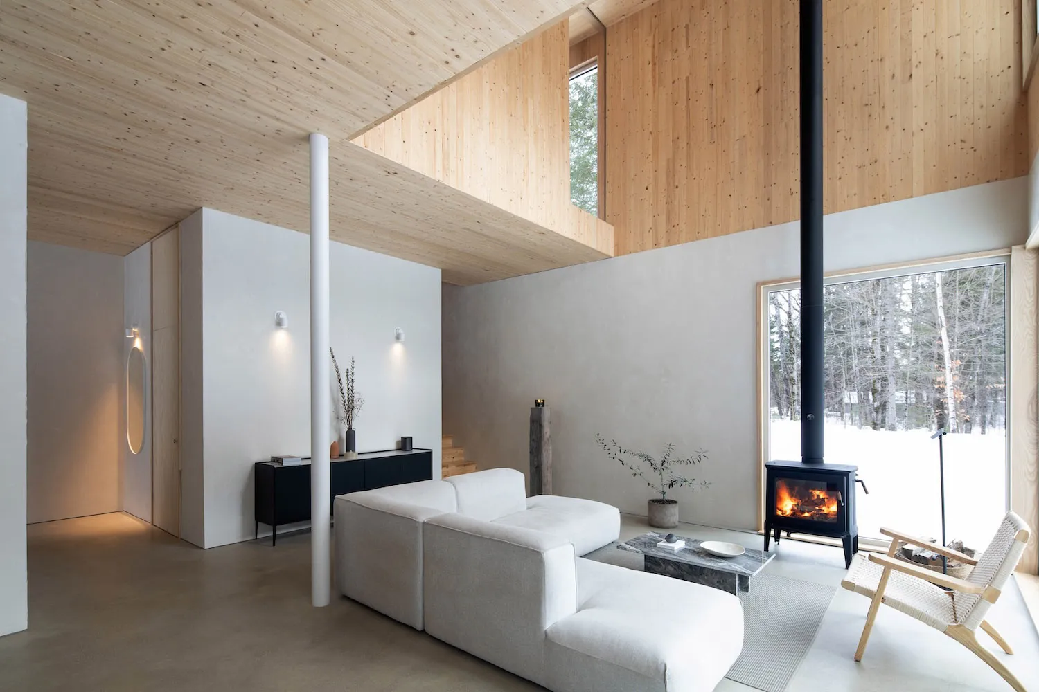 Modern minimalist living room with white furniture, concrete floor, wood paneling, and a fireplace.