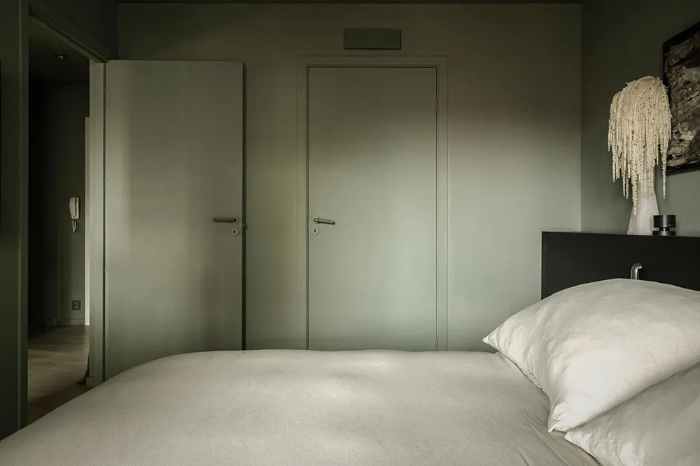 Minimalist bedroom with neutral tones, featuring a large bed, white pillows, and two green doors.