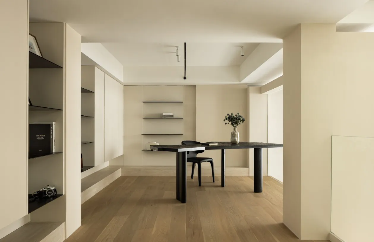 A minimalist home office featuring a black metal table and a vase of greenery.