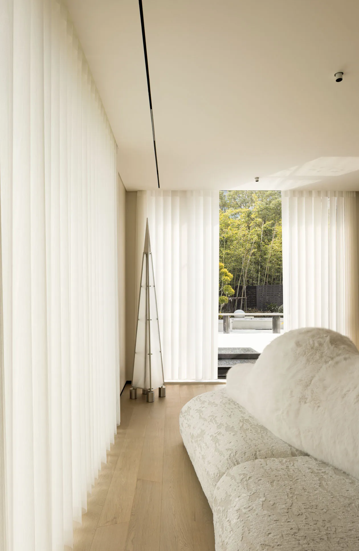 Modern minimalist living room featuring a fabric sofa, wooden floor, and glass divider.