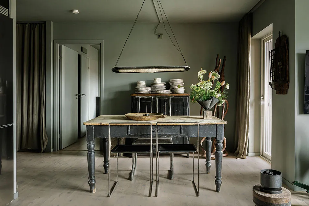 A rustic dining room featuring wooden furniture, plates stacked on a wooden sideboard, and a hanging light fixture.