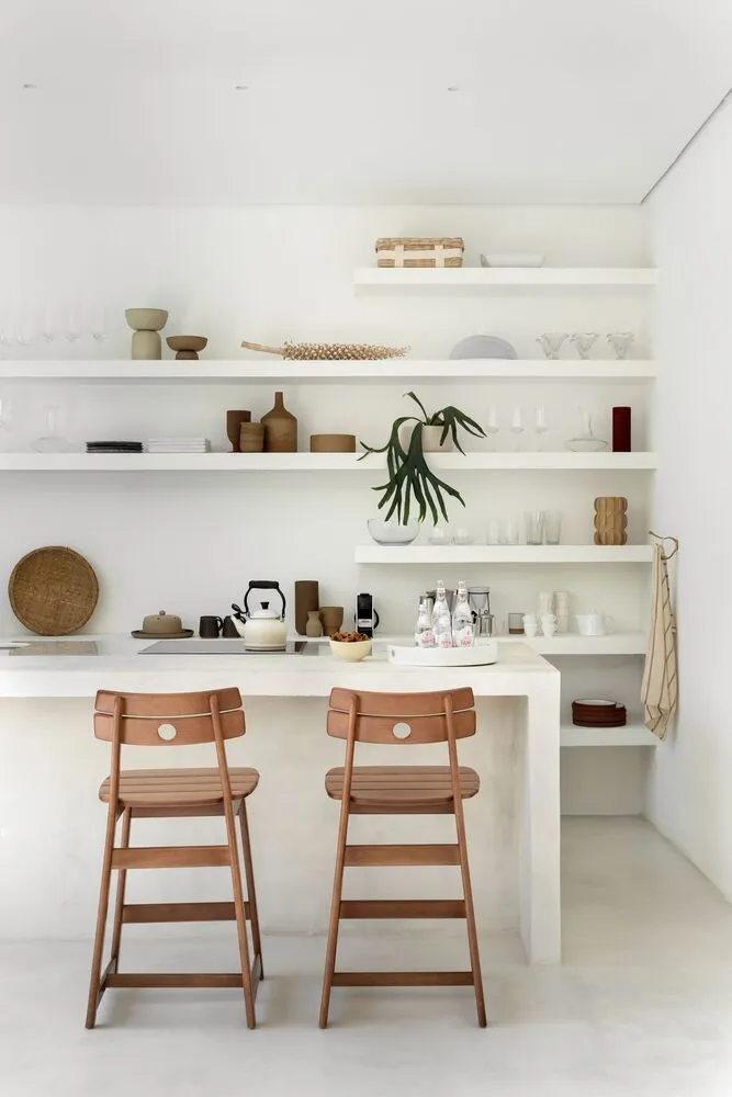 A minimalist interior with a white space, wooden chairs, and floating shelves.