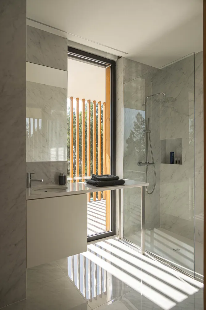 A modern bathroom with marble walls and floor, featuring a glass shower enclosure and a window with natural light.