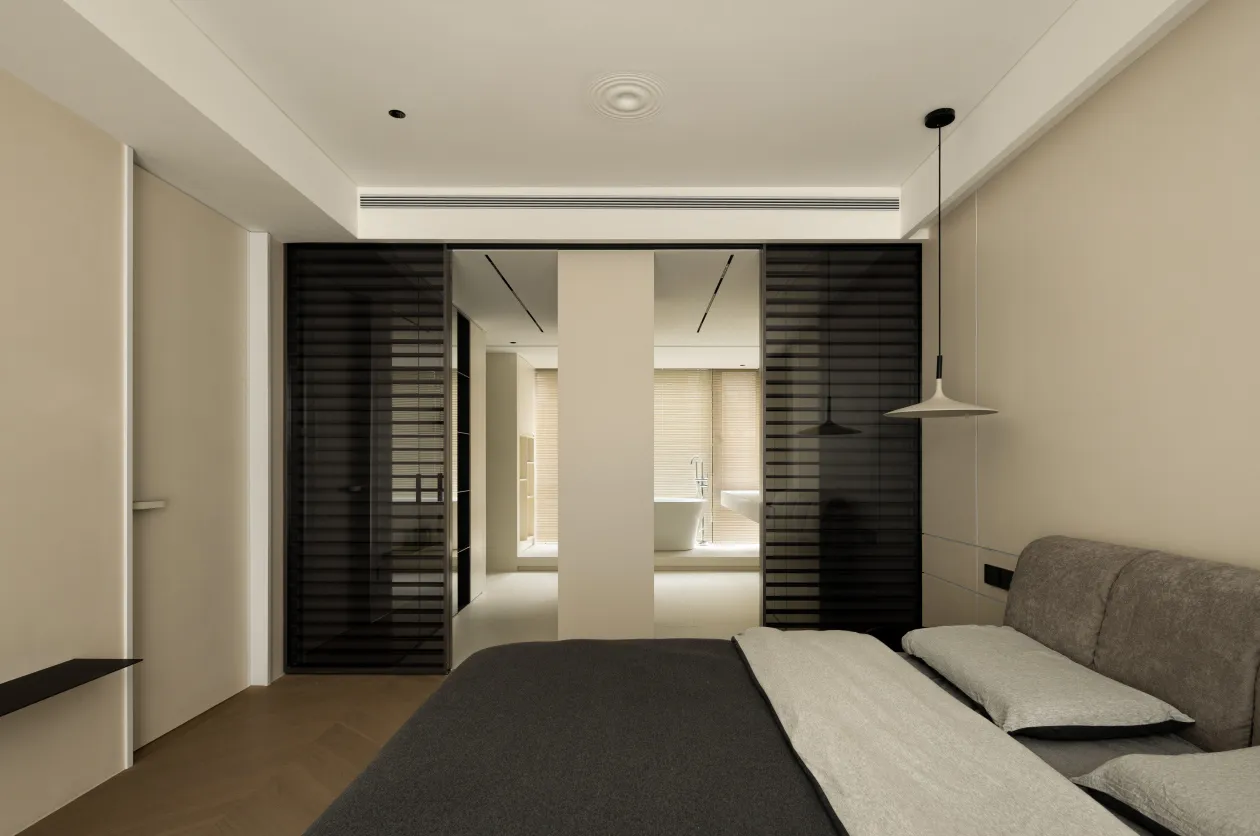 A minimalist bedroom with a bed, a sofa, and black blinds in a neutral-colored room