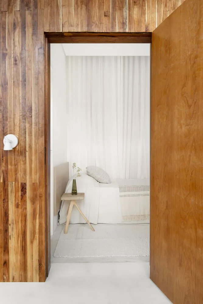 Minimalist bedroom featuring wooden walls and white bedding with a vase of flowers on a small table.