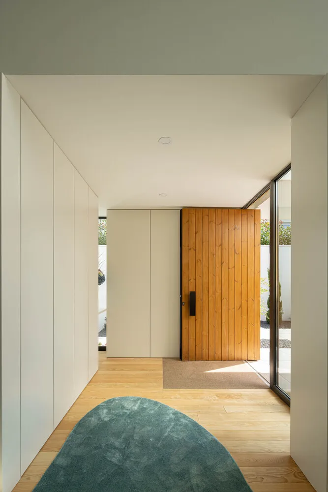Minimalist entryway with hardwood flooring and wooden door, featuring a light blue rug and a window with white trim.