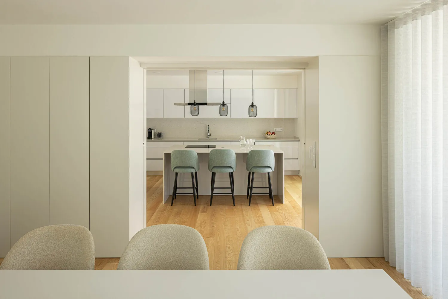 Modern kitchen featuring white cabinets, countertop, and bar stools with green accents.