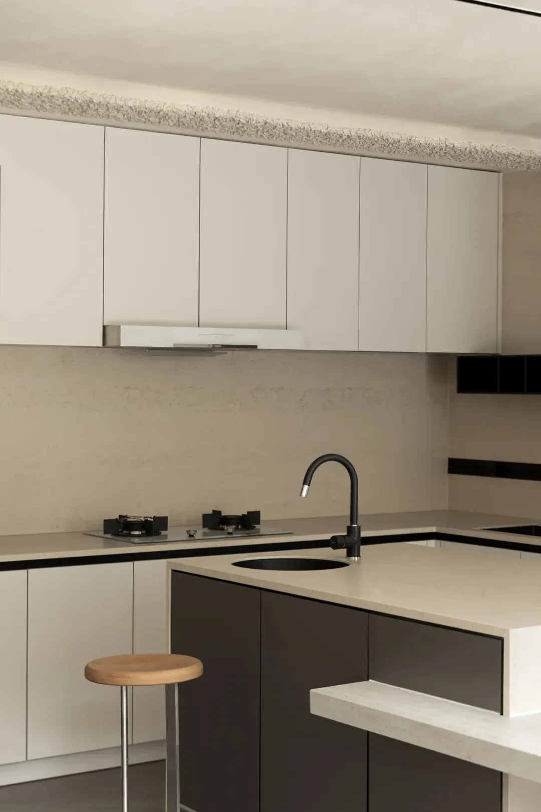 Modern kitchen featuring concrete countertops with black fittings and a wooden stool.