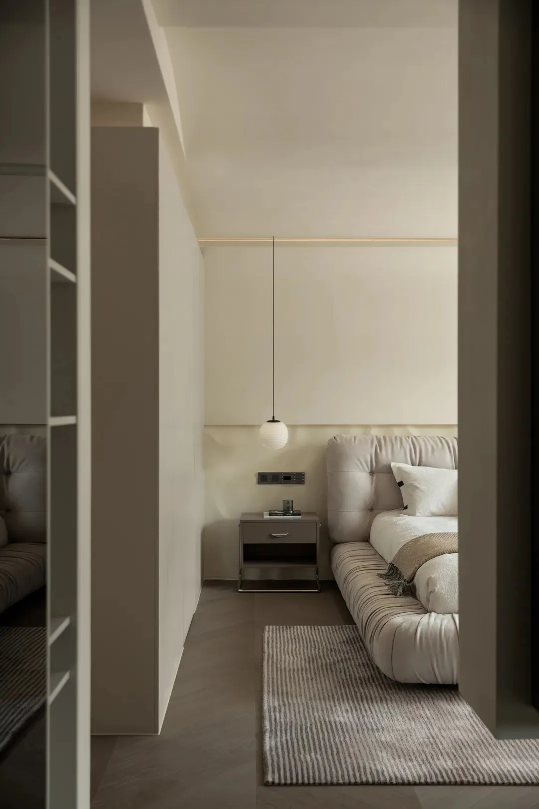 A minimalist bedroom featuring neutral-toned furnishings and a hanging pendant light.