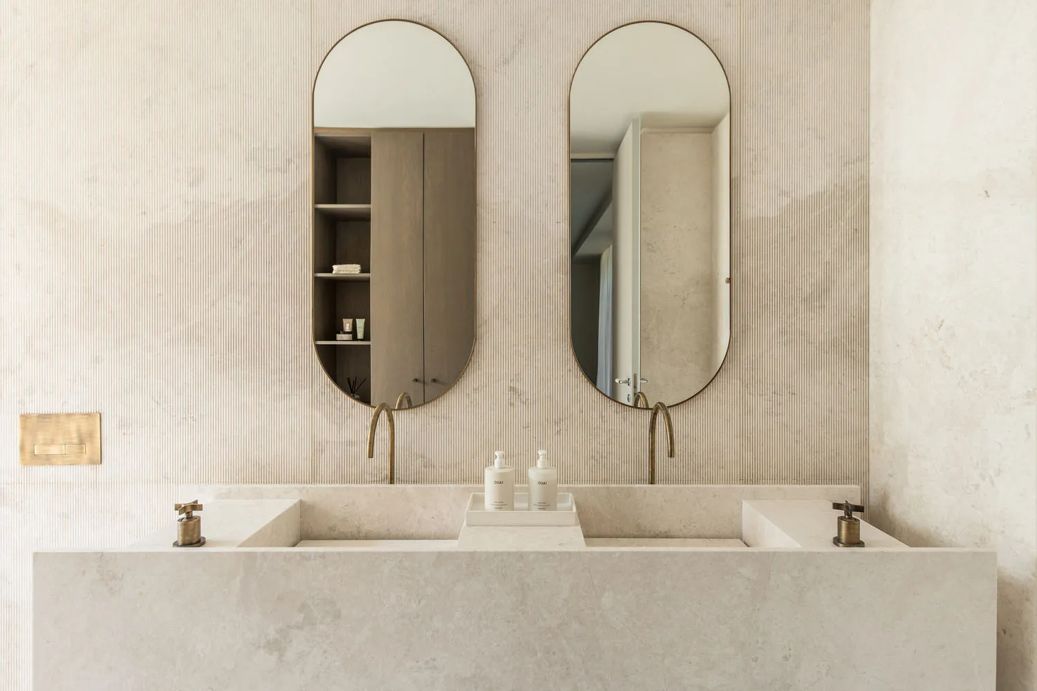 Modern minimalist bathroom with marble countertops and sinks, featuring brass faucets and a light-colored textured wall.